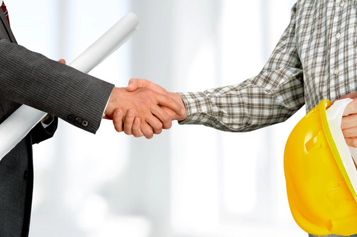 Handshake between businessman and construction worker with yellow hard hat showing trusted partnership with Buildwell pan India presence and distribution