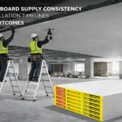 Construction workers installing gypsum boards on a false ceiling frame using ladders with stacked drywall sheets on site – Best Gypsum Board Supplier in India